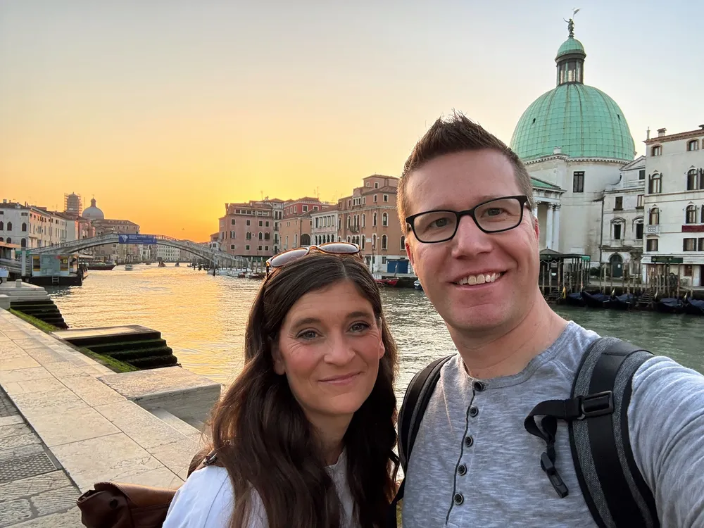 Emily and Josh on the Grand Canal at sunrise, the water gold and the green dome of San Simeone Piccolo behind them