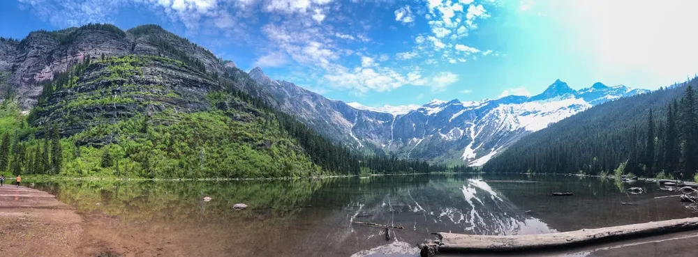A wide view of Avalanche Lake, still water reflecting the cliffs and the snowfields at the head of the valley