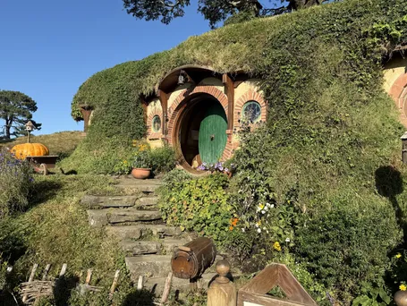 Bag End, the green round door under the brick arch set into the grassy hill, stone steps leading up to it and a pumpkin in a barrow to the left