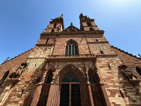 The red sandstone front of Basel Minster from below, its two spires and rose window against a clear sky