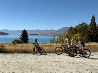 Josh and three of the children on mountain bikes on a gravel track above the turquoise lake, dry hills and mountains behind