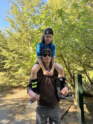 Preston carrying Case on his shoulders on a bush trail, holding Case's walking boot in one hand