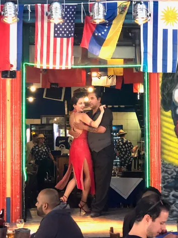 A tango show in a Buenos Aires bar with a man and woman dancing in embrace under flags from a dozen countries