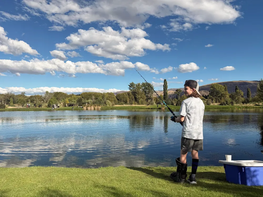 Case fishing from the bank of a stocked pond with his rod bent, in a backwards cap and a walking boot