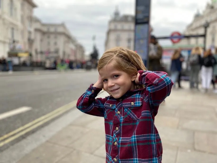 Case grinning on a London street with his hands behind his head, an Underground sign and Regent Street buildings behind him