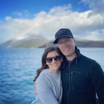 Emily and Josh together on the catamaran deck with a rainbow arcing over the hills behind them