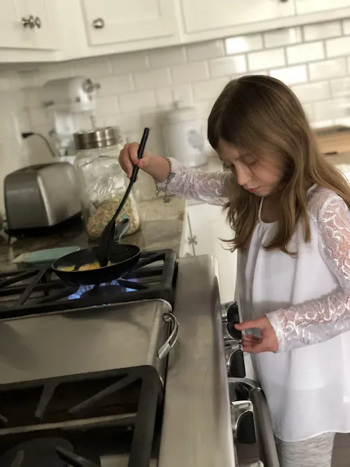 Evie at the gas hob turning eggs in a small frying pan with a spatula