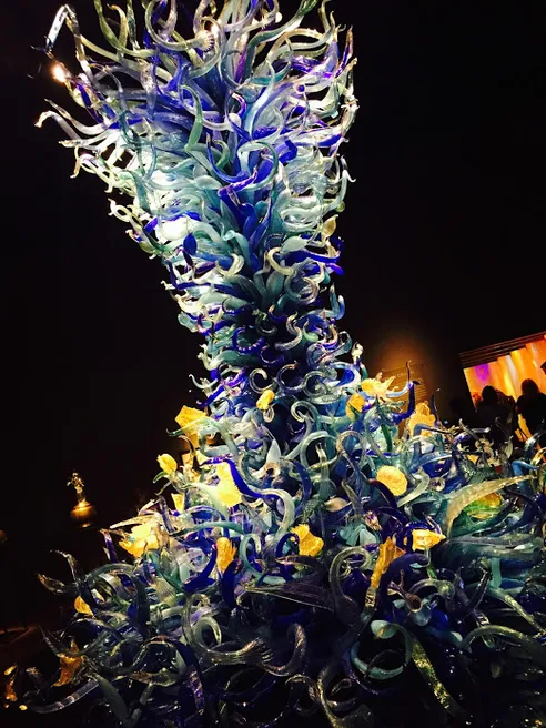 A towering Chihuly sculpture of curling blue and yellow blown glass lit against a black room