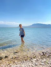 Mia standing ankle deep in the clear shallows of the reservoir, flat-topped hills across the water