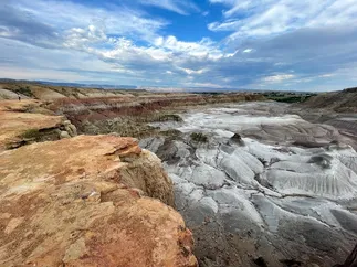 The eroded grey and rust badlands of Devils Kitchen under a big streaked sky