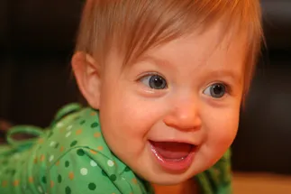 Evie as a baby in a green polka dot top, laughing with her first teeth showing