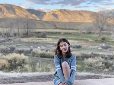 Evie sitting on the patio wall at the ranch, the Big Horn escarpment lit gold behind her