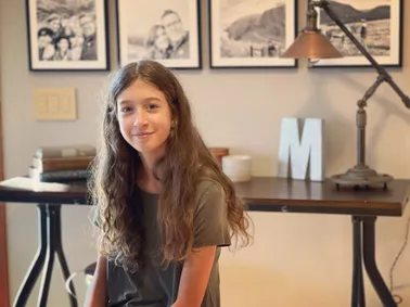 Evie with her hair long and loose in the study, framed family photographs on the wall behind her
