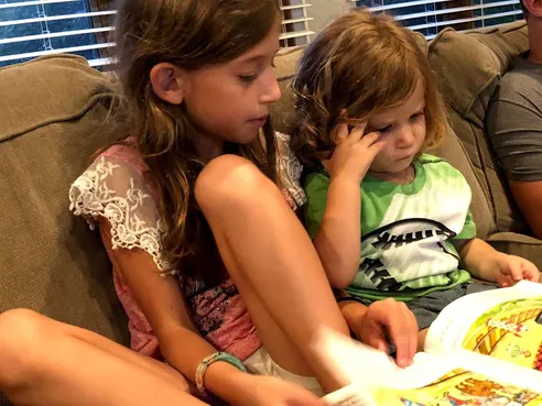 One of the girls reading a picture book on the sofa with Case leaning into her shoulder