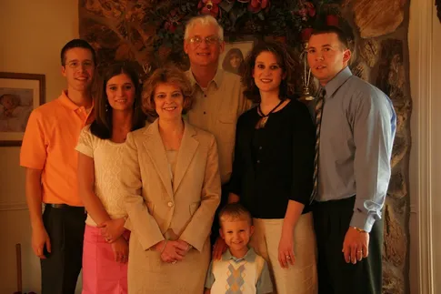 The extended family posed together by the stone fireplace, the youngest boy in a blue argyle vest at the front