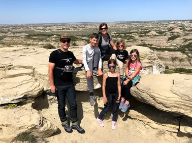 All six of them on a flat sandstone outcrop, the layered badlands stretching to the horizon behind