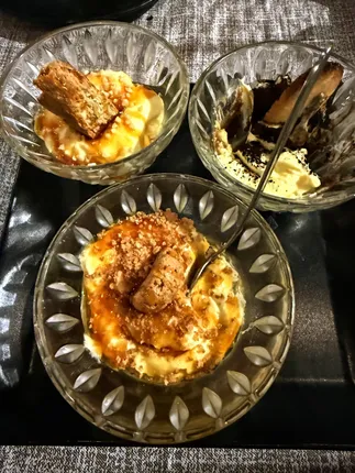 Three glass dishes of tiramisu on a dark tray, two barely touched and one half eaten