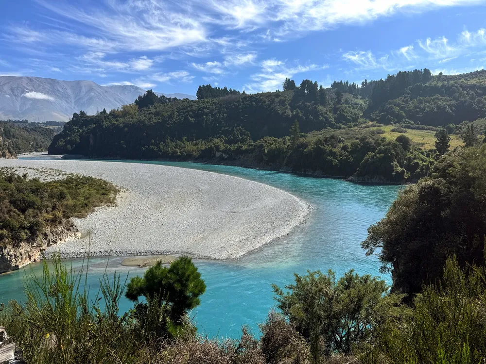 A bright turquoise river curving round a wide pale shingle bank in the Rakaia gorge, native bush on the banks and mountains beyond