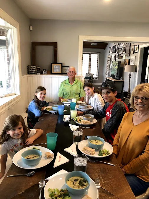 The four children at the dining table with both grandparents, bowls of soup and sandwiches in front of everyone