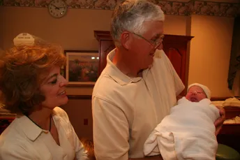 Emily's parents looking down at a newborn wrapped in white in her father's arms