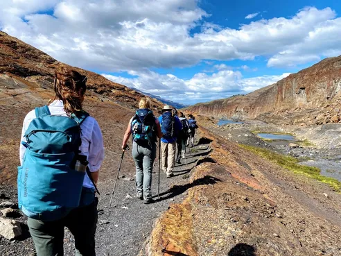 A line of hikers with backpacks walking into a canyon with fossil rock formations on either side