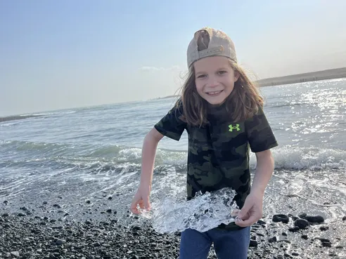 Case grinning on the black pebbles holding up a clear slab of glacier ice with both hands