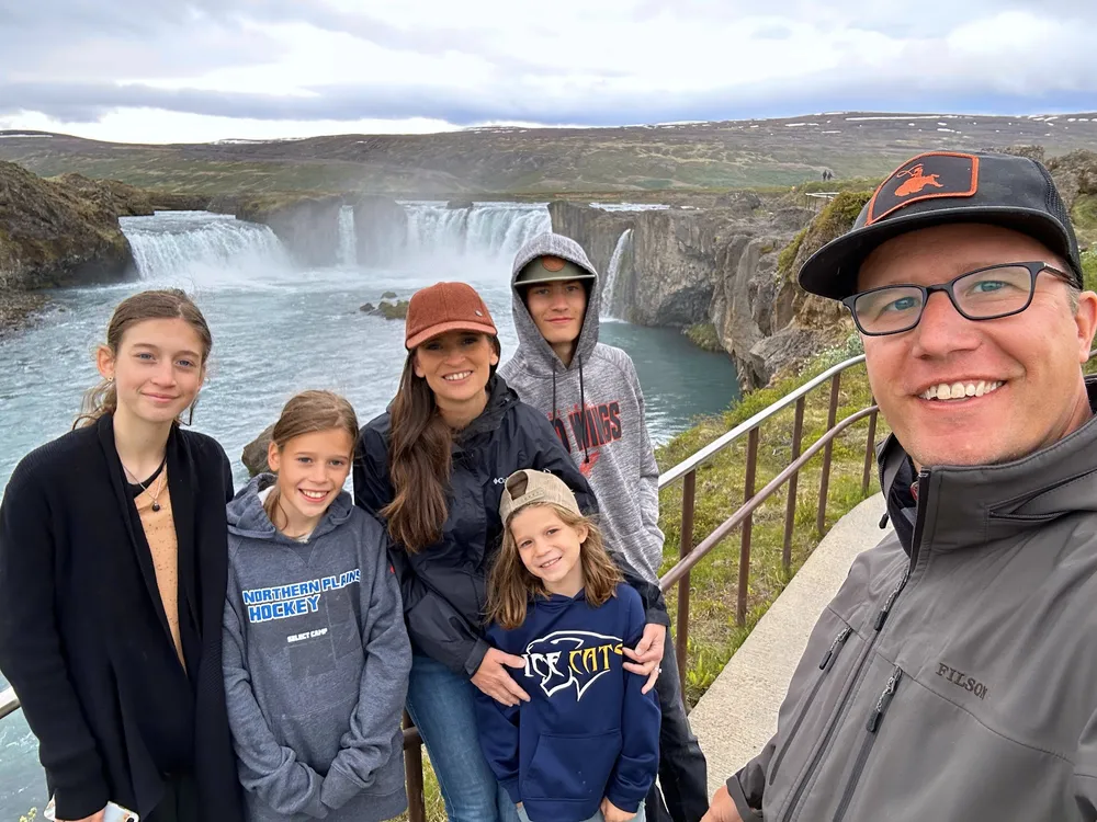 All six of them at the rail above Godafoss, the broad curved falls and turquoise river behind them