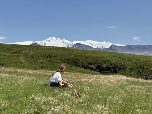 Mia sitting in long grass looking out at the snow-covered ice cap above the green scrub of the national park