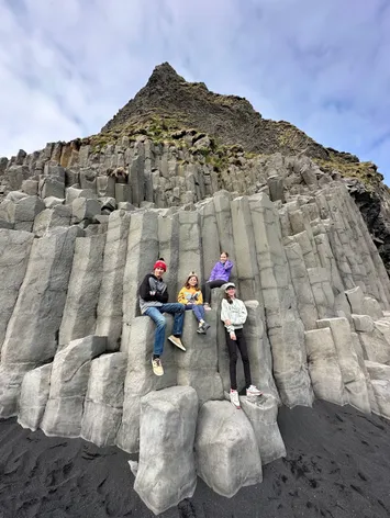 The four children sitting and standing on the stepped basalt columns at Reynisfjara, the black sand beach below them