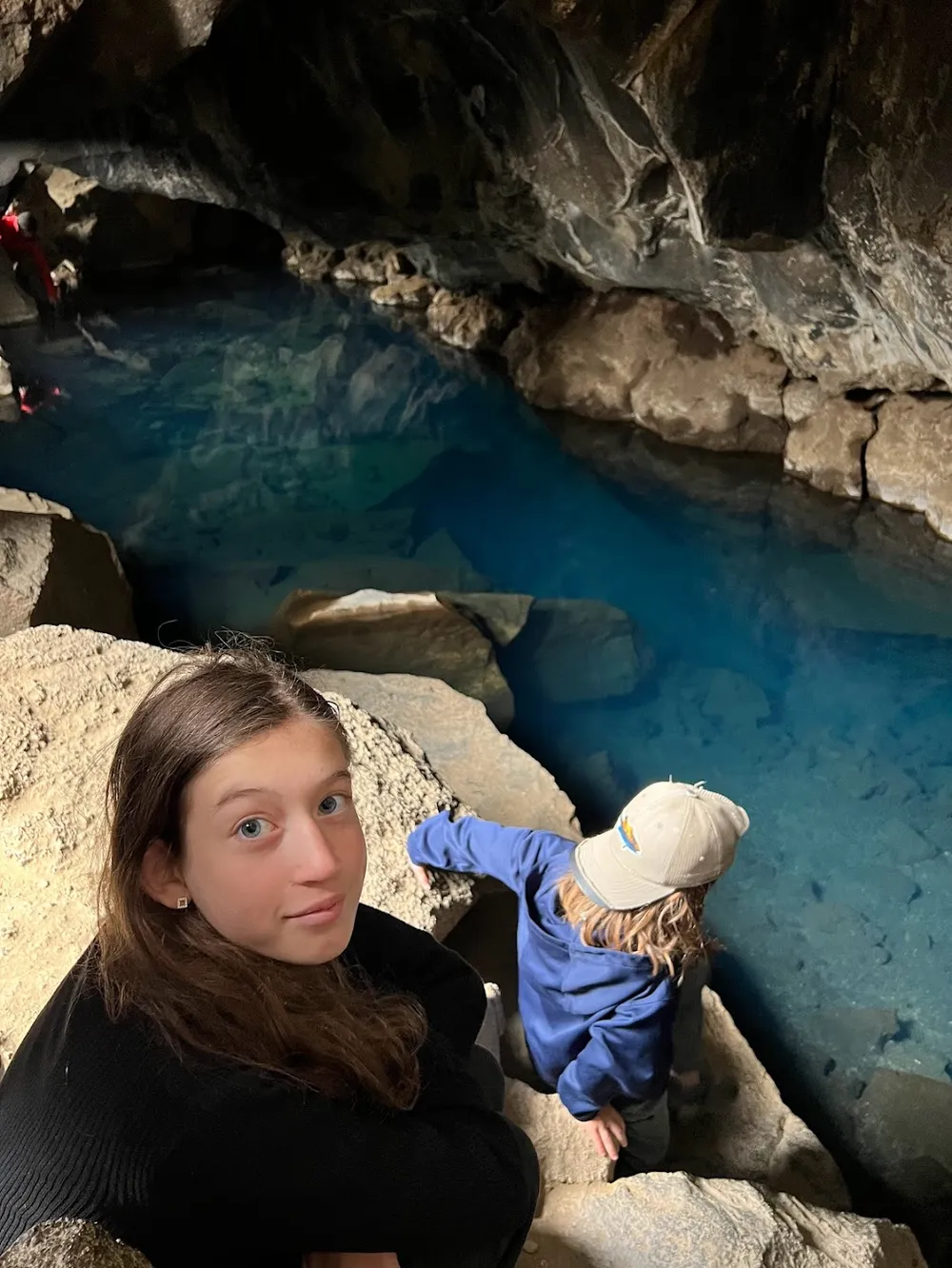 Two of the children on the rocks inside Grjotagja, the bright blue geothermal pool filling the lava cave beside them