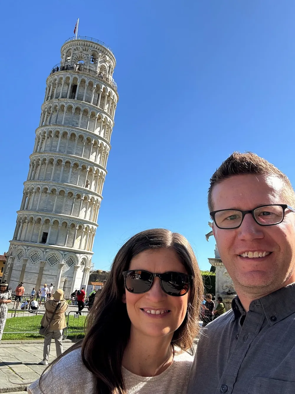 Emily and Josh in sunglasses in front of the Leaning Tower of Pisa against a cloudless blue sky
