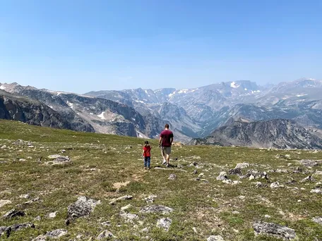 Josh and Case walking away across high alpine tundra, a vast range of grey peaks and cirques spread below them