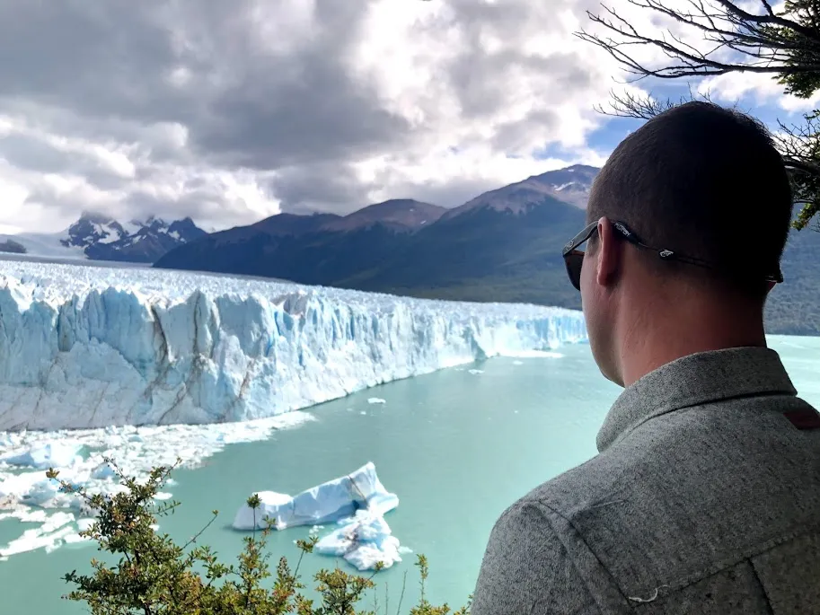Josh in the foreground looking out at the blue wall of the Perito Moreno glacier, icebergs in the pale green water below