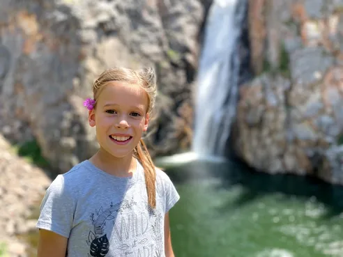 Mia with a pink flower behind her ear in front of Porcupine Falls, the water dropping into a green pool