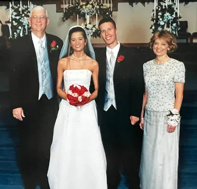 Emily and Josh on their wedding day standing between her parents, Emily holding a bouquet of red and pink roses