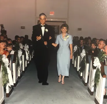 Emily's parents walking back down the aisle together, her father carrying a lit candle, guests in the pews either side