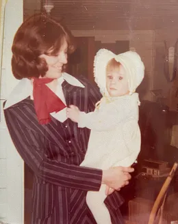 Emily's mother in a pinstriped suit holding her baby daughter in a knitted bonnet