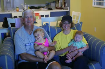 Emily's parents on a striped sofa, each holding a grandchild on their lap