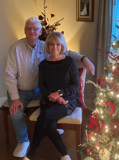 Emily's parents on a bench beside the lit Christmas tree, their wedding portrait hanging on the wall behind