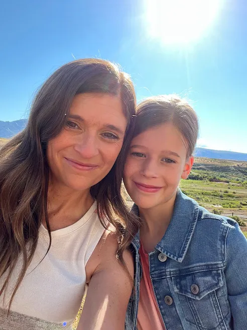 Emily and Mia cheek to cheek in the sun, the valley and hills behind them