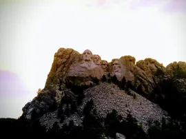 The four presidents carved into the granite of Mount Rushmore, seen from below against a pale sky