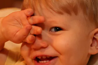 Preston as a baby laughing with his hand up over one eye, his first teeth showing