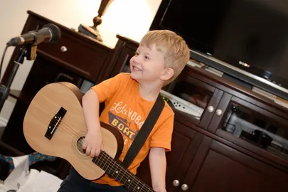 Preston as a small boy in an orange t-shirt with a guitar on a strap, singing into a microphone on a stand