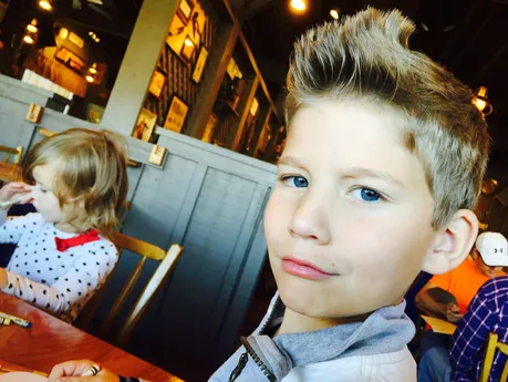 Preston close to the camera in a restaurant with his hair up in a quiff, one of his sisters colouring at the table behind