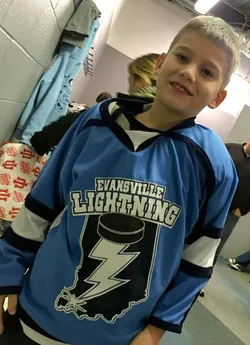 Preston holding up a pale blue Evansville Lightning hockey jersey in the changing room