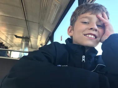 Preston leaning back in a train seat with his hand in his hair, laughing at the camera