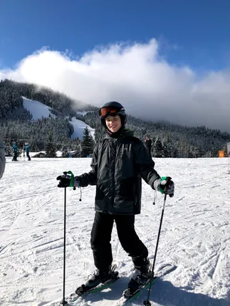 Preston on skis in helmet and goggles at the bottom of the piste, cloud rolling off the forested mountain behind