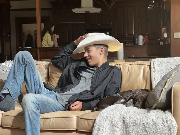 Preston stretched out on the sofa in a white cowboy hat with the dog asleep beside him