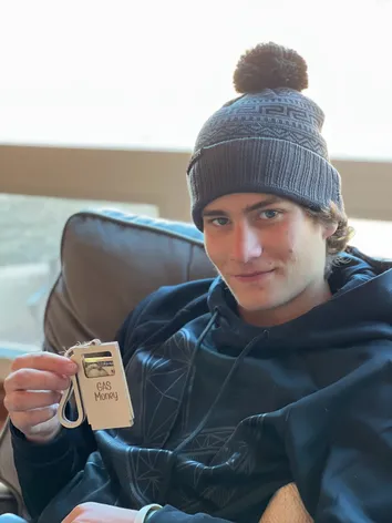 Preston in a bobble hat holding up a card wallet labelled Gas Money with a note tucked in it
