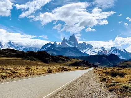 An empty road running towards the jagged spires of Mount Fitz Roy under a big cloudy sky